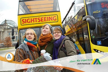 Passvorteil | Drei Menschen, die nach vorne schauen, vor einem gelben Aussichtsbus,